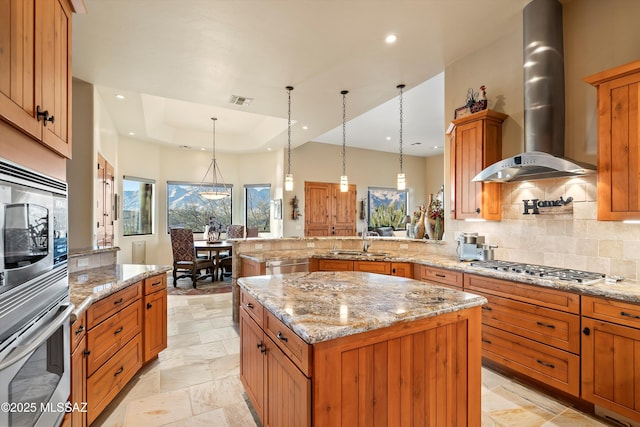 kitchen with pendant lighting, a center island, wall chimney range hood, stainless steel appliances, and sink