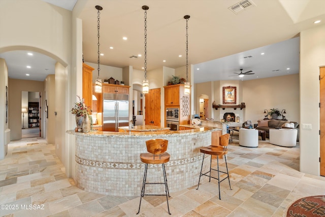 kitchen with built in appliances, a towering ceiling, light stone countertops, kitchen peninsula, and pendant lighting