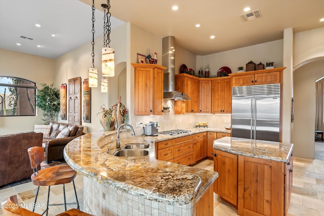 kitchen with a kitchen island, wall chimney range hood, stainless steel appliances, sink, and kitchen peninsula