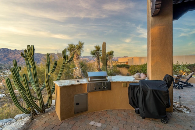 patio terrace at dusk featuring a mountain view, an outdoor kitchen, and grilling area