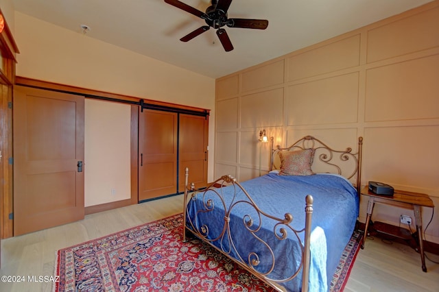 bedroom with a barn door, light hardwood / wood-style flooring, and ceiling fan