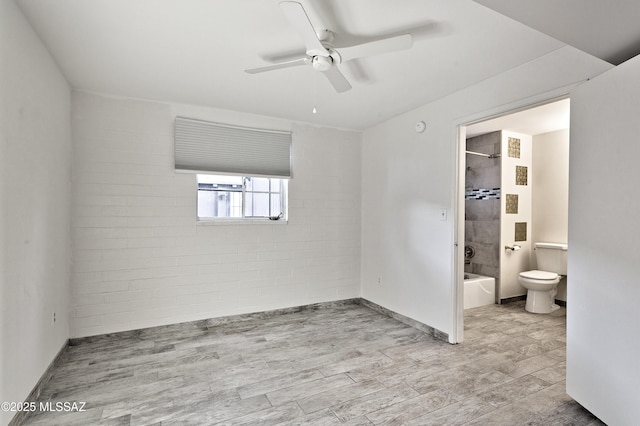 unfurnished bedroom with light wood-type flooring, ensuite bathroom, ceiling fan, and brick wall