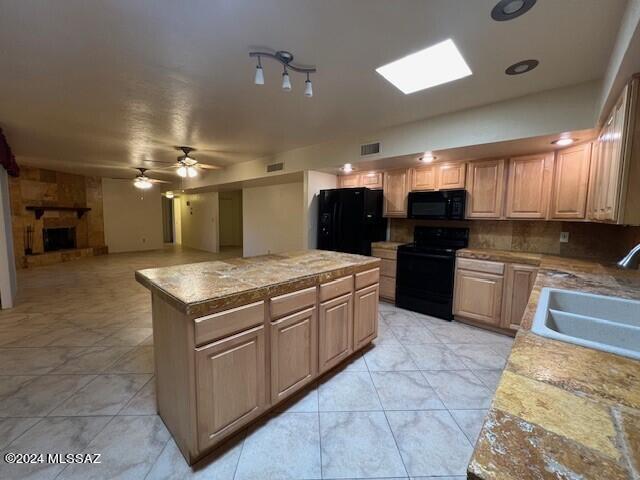 kitchen with a center island, black appliances, sink, ceiling fan, and a large fireplace