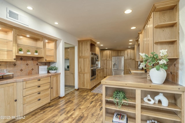 kitchen with light brown cabinetry, appliances with stainless steel finishes, decorative backsplash, and hardwood / wood-style floors