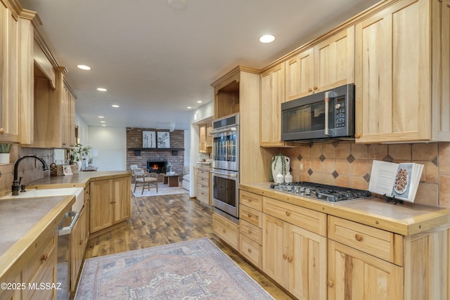 kitchen featuring hardwood / wood-style flooring, appliances with stainless steel finishes, light brown cabinets, backsplash, and a fireplace