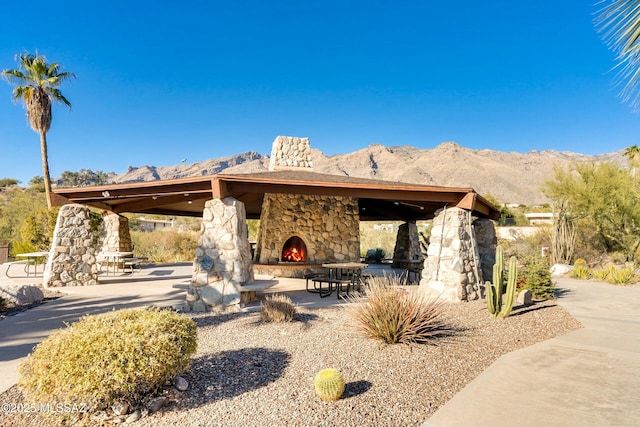 rear view of house with a patio area, an outdoor stone fireplace, and a mountain view