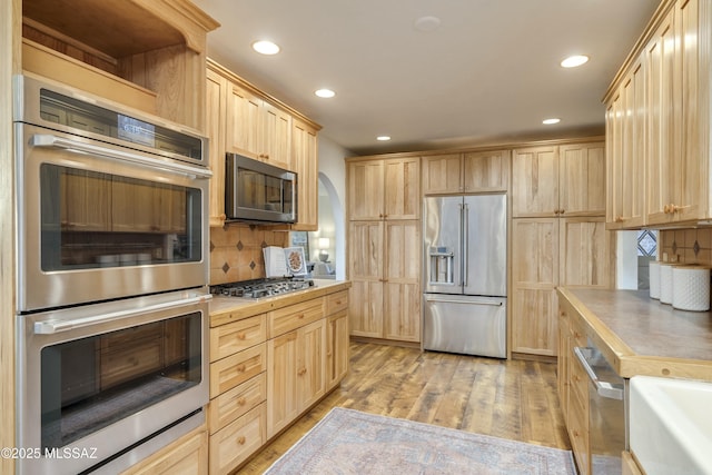 kitchen featuring light brown cabinets, appliances with stainless steel finishes, decorative backsplash, and light hardwood / wood-style flooring