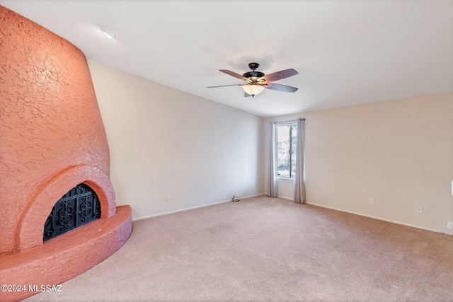 unfurnished living room featuring light carpet, a large fireplace, and ceiling fan