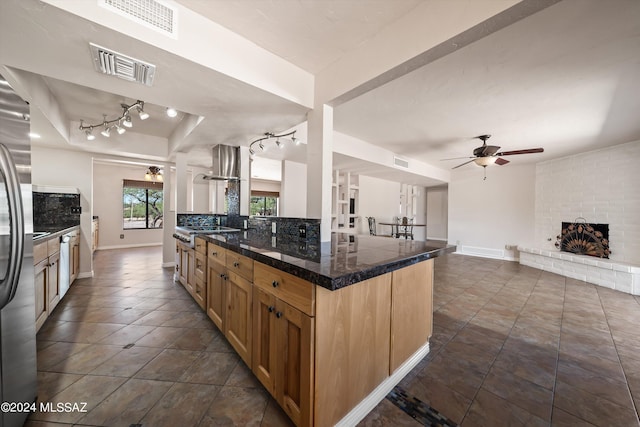 kitchen with kitchen peninsula, stainless steel fridge, tasteful backsplash, a brick fireplace, and ceiling fan