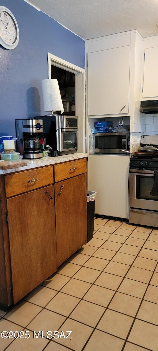 kitchen featuring decorative backsplash, stainless steel appliances, white cabinetry, and light tile patterned flooring