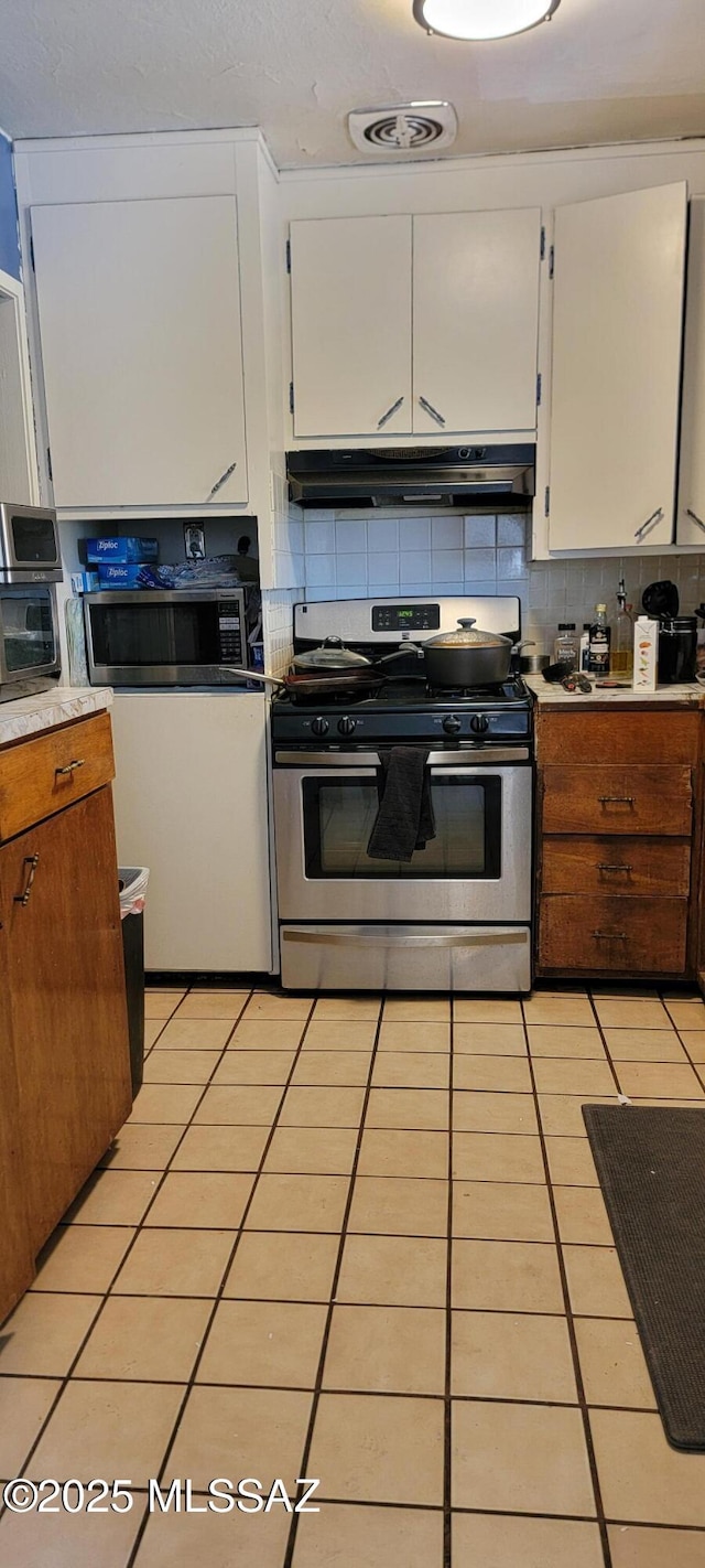 kitchen featuring tasteful backsplash, white cabinetry, light tile patterned flooring, and appliances with stainless steel finishes