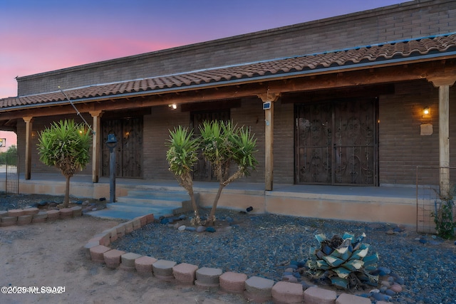 property entrance featuring covered porch, brick siding, and a tiled roof