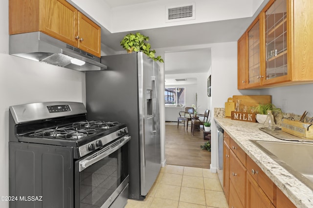 kitchen with light stone countertops, sink, light tile patterned floors, and appliances with stainless steel finishes