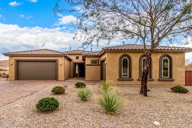 mediterranean / spanish home featuring decorative driveway, a tile roof, an attached garage, and stucco siding