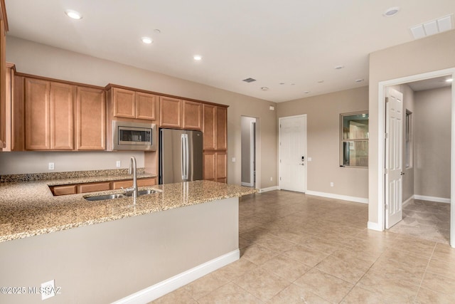 kitchen with visible vents, brown cabinets, light stone counters, a sink, and appliances with stainless steel finishes