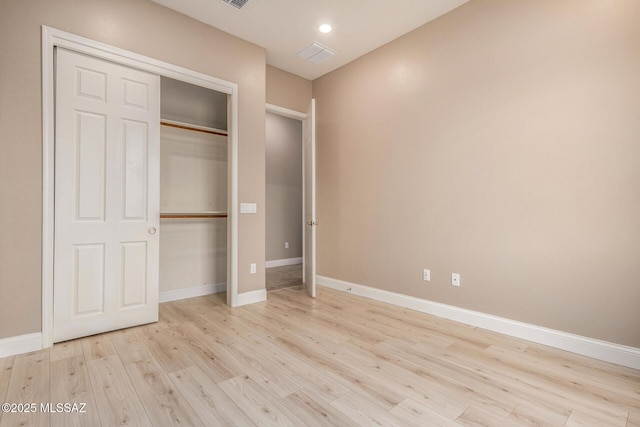 unfurnished bedroom featuring baseboards, light wood-style flooring, visible vents, and a closet
