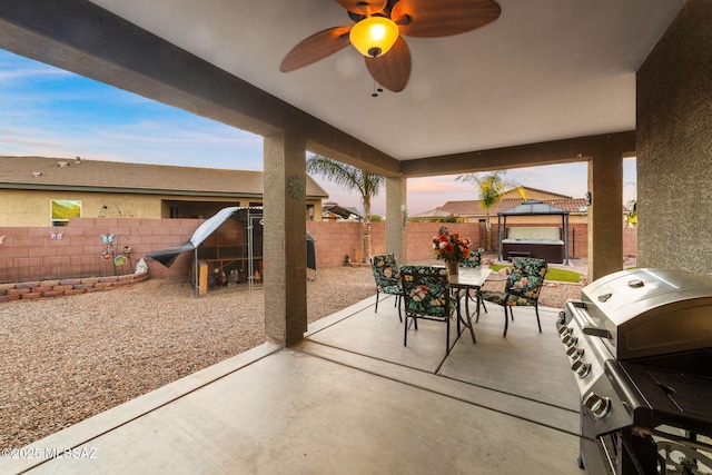 patio terrace at dusk featuring grilling area, ceiling fan, and a hot tub