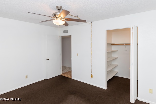 unfurnished bedroom with ceiling fan, a closet, a textured ceiling, and dark colored carpet