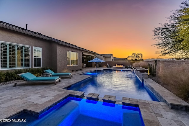 pool at dusk featuring a patio area, pool water feature, and a jacuzzi