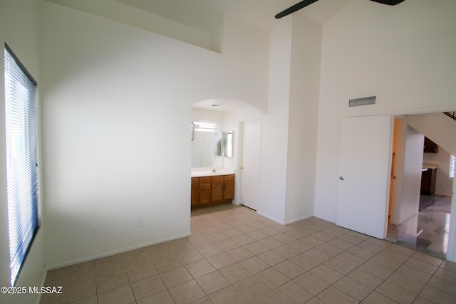 empty room with arched walkways, ceiling fan, light tile patterned floors, a towering ceiling, and visible vents