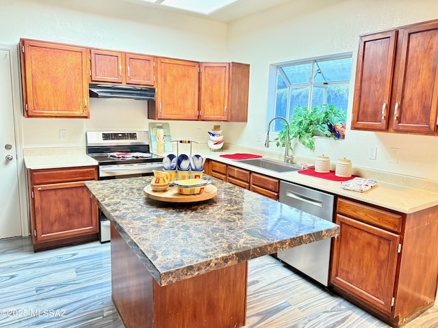 kitchen featuring a center island, stainless steel appliances, brown cabinetry, a sink, and under cabinet range hood