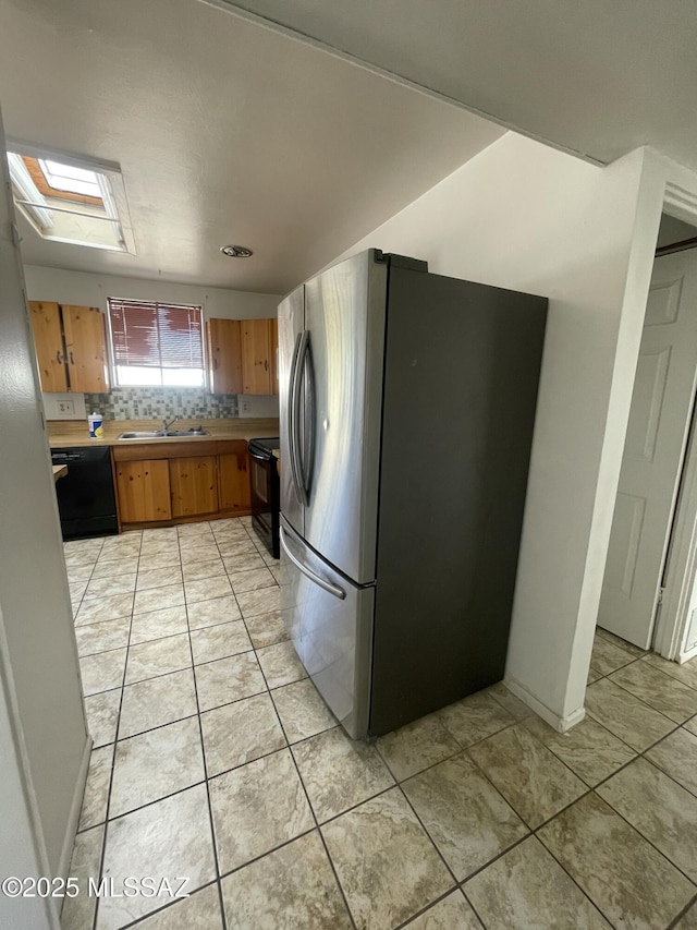 kitchen featuring backsplash, black appliances, sink, a skylight, and light tile patterned floors