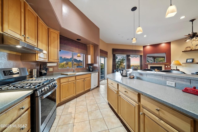 kitchen with pendant lighting, white dishwasher, a tiled fireplace, ceiling fan, and stainless steel range with gas stovetop