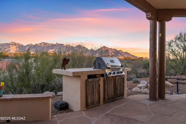 patio terrace at dusk featuring grilling area, exterior bar, a mountain view, and area for grilling