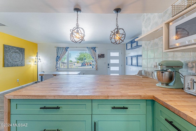 kitchen with butcher block counters, stainless steel microwave, backsplash, pendant lighting, and green cabinetry