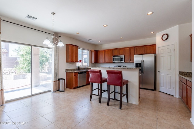 kitchen featuring appliances with stainless steel finishes, light stone counters, a kitchen island, a breakfast bar area, and light tile patterned flooring