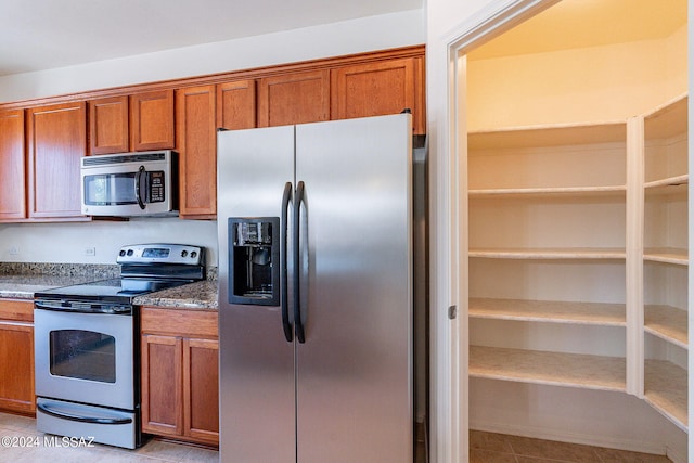 kitchen with dark stone countertops, light tile patterned floors, and stainless steel appliances