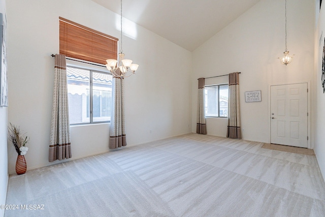 carpeted spare room featuring a wealth of natural light, high vaulted ceiling, and a notable chandelier