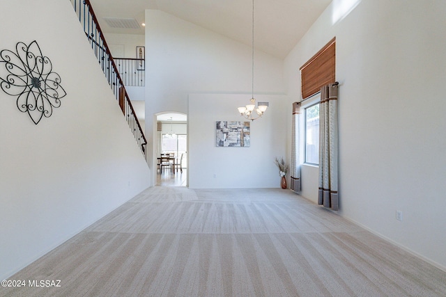 unfurnished living room with light carpet, plenty of natural light, high vaulted ceiling, and an inviting chandelier