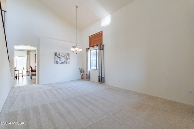 carpeted spare room featuring a chandelier, high vaulted ceiling, and a healthy amount of sunlight