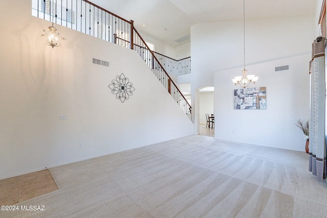 unfurnished living room with a towering ceiling, light carpet, and a chandelier