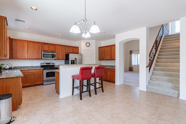 kitchen with a center island, an inviting chandelier, appliances with stainless steel finishes, decorative light fixtures, and light stone counters