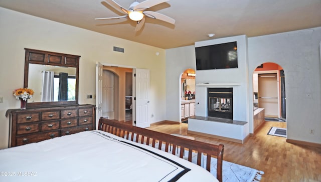 bedroom with a multi sided fireplace, ensuite bathroom, ceiling fan, and light hardwood / wood-style floors