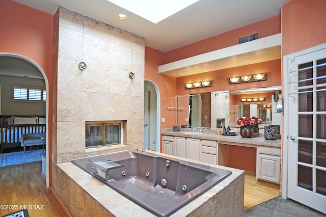 bathroom featuring vanity, a tile fireplace, and tiled tub