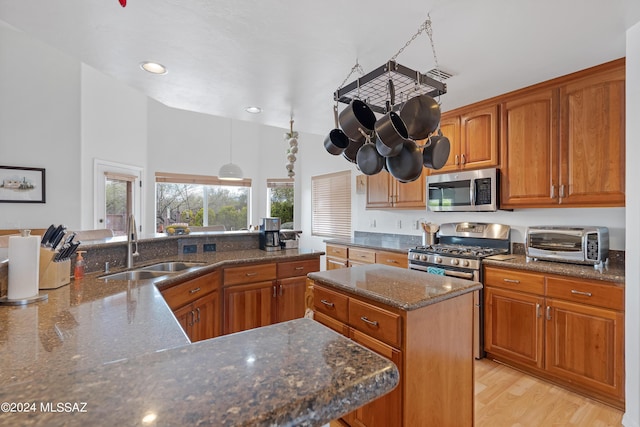 kitchen with appliances with stainless steel finishes, light wood-type flooring, dark stone counters, sink, and a center island