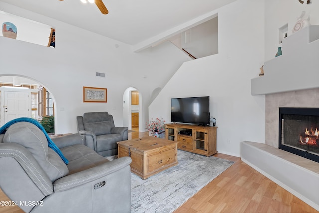 living room featuring a tile fireplace, a high ceiling, light hardwood / wood-style floors, and ceiling fan