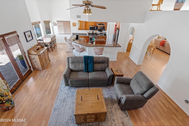 living room featuring ceiling fan, a high ceiling, and light wood-type flooring