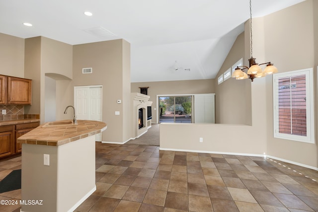 kitchen with tile countertops, lofted ceiling, sink, hanging light fixtures, and decorative backsplash