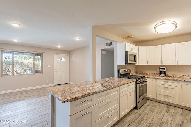 kitchen featuring white cabinetry, light hardwood / wood-style flooring, appliances with stainless steel finishes, kitchen peninsula, and light stone countertops