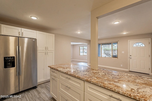 kitchen with stainless steel refrigerator with ice dispenser, light stone countertops, light wood-type flooring, and white cabinets