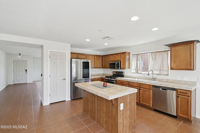 kitchen with a center island, sink, light tile patterned floors, appliances with stainless steel finishes, and tile counters