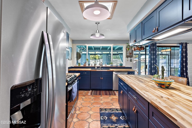 kitchen with sink, blue cabinetry, wooden counters, stainless steel appliances, and decorative light fixtures