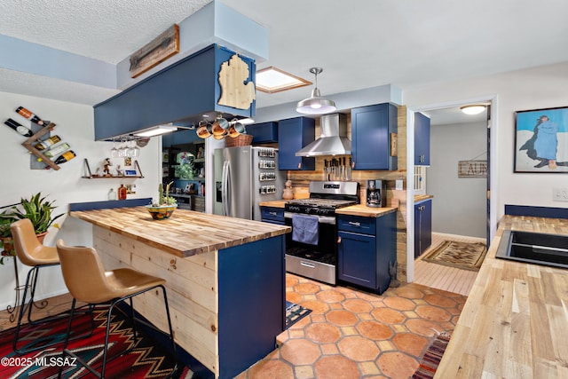 kitchen featuring blue cabinetry, appliances with stainless steel finishes, a breakfast bar area, and wall chimney range hood