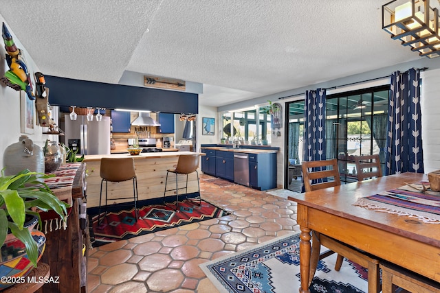 kitchen with blue cabinets, a breakfast bar area, appliances with stainless steel finishes, kitchen peninsula, and wall chimney range hood