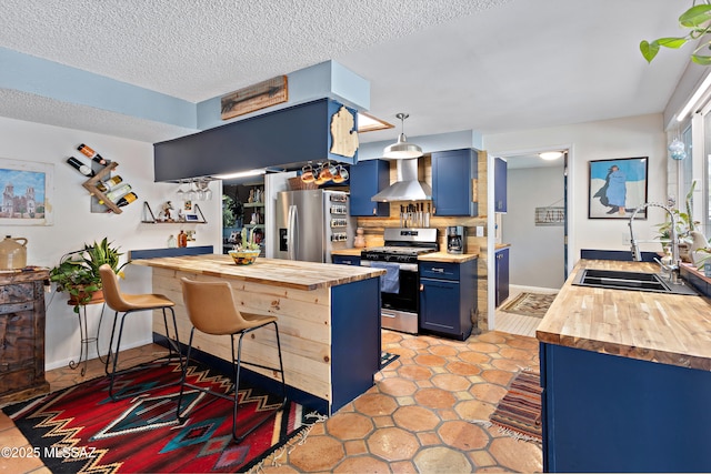 kitchen featuring butcher block countertops, sink, blue cabinetry, stainless steel appliances, and wall chimney exhaust hood