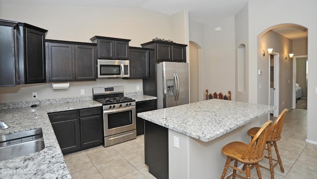 kitchen featuring light stone countertops, appliances with stainless steel finishes, sink, light tile patterned floors, and a kitchen island